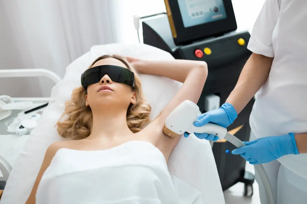 Woman receiving underarm laser hair removal treatment from a technician in a professional med spa setting.
